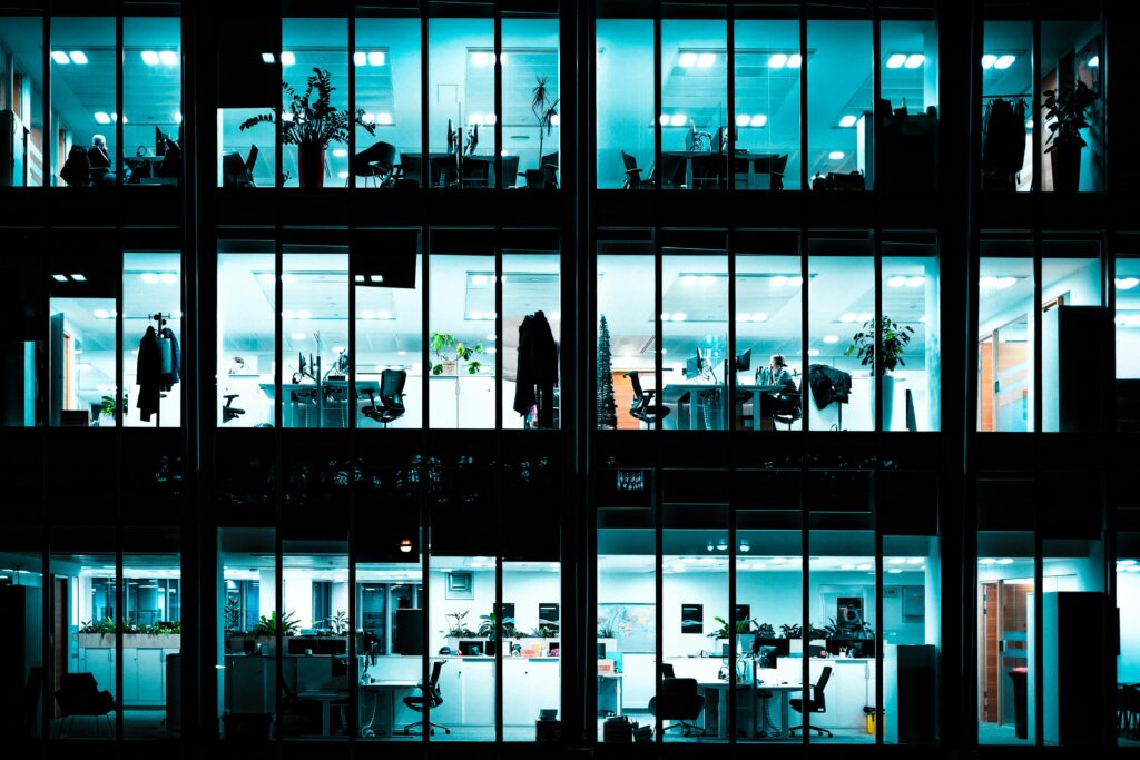 Night view of an illuminated modern office building showcasing workspaces through large windows.